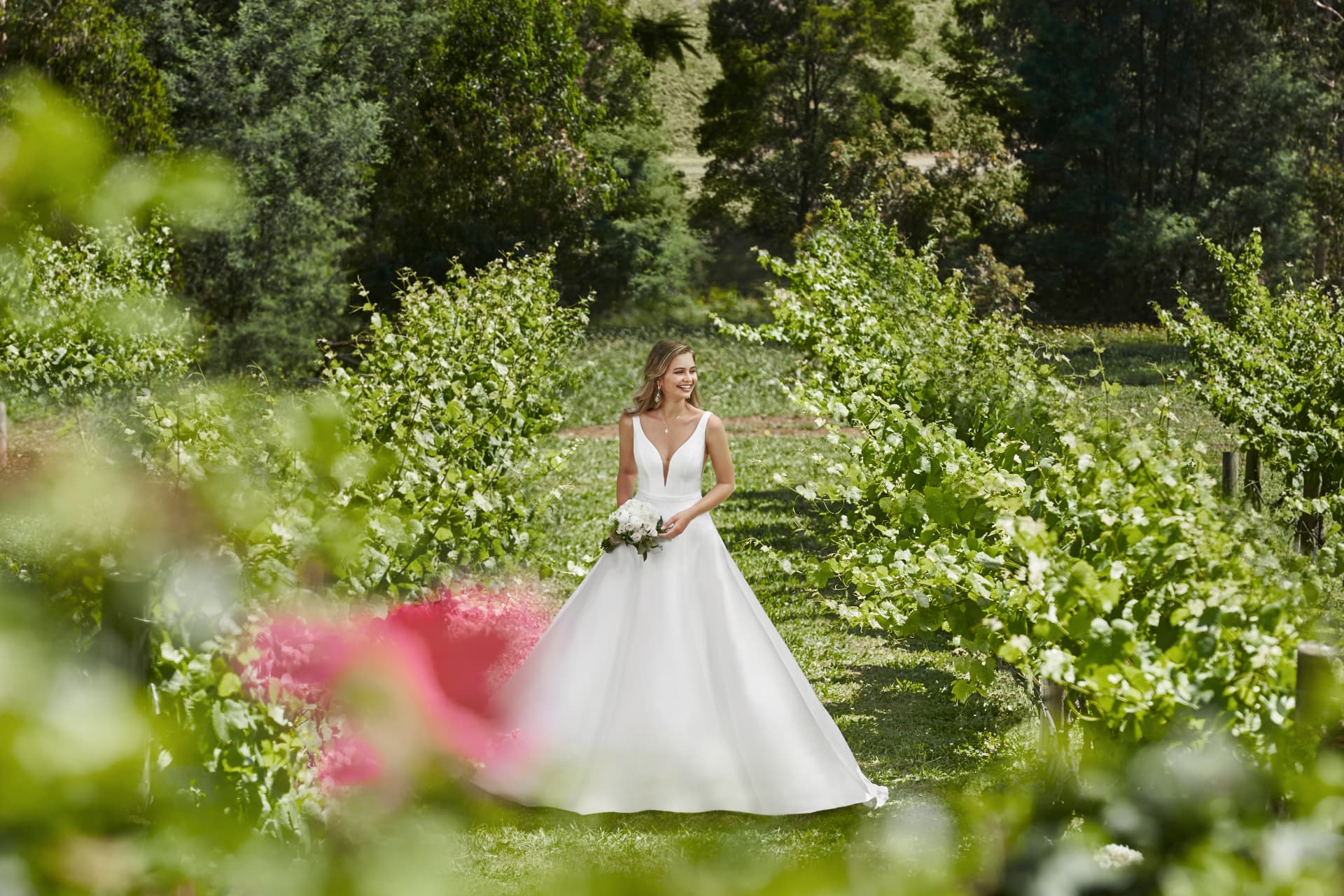 Noiva sorrindo com vestido de noiva de alças em jardim verde